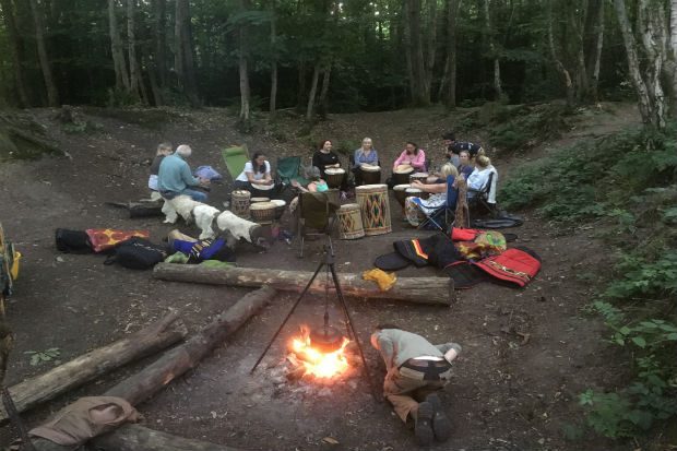 A group of people sitting in a circle in a forest with a burning stove beside them