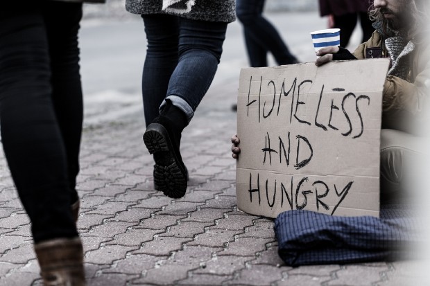 People walking passed a homeless person who is begging and in need of food