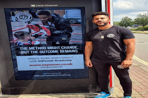 Daryl standing by a billboard with the slogan 'The method might change but the outcome remains'