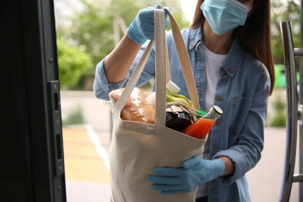 Female volunteer giving bag with products through doorway, closeup. Aid during coronavirus quarantine